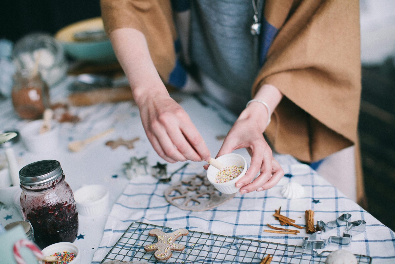 Woman decorating homemade gingerbread cookies with sprinkles in a cozy kitchen.